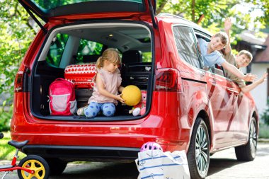 Yaz tatiline çıkmadan önce arabada oturan üç çocuk, iki oğlan ve iki anaokulu kızı. Mutlu çocuklar, kardeşler, bavulları ve oyuncakları olan kız ve erkek kardeşler aile yolculuğuna çıkıyorlar.