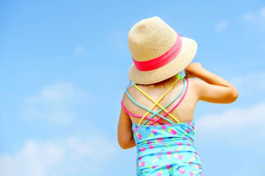 Renkli mayo ve hasır şapkalı anaokulu kızının portresi. Deniz kenarında aile tatiline çıkmış tatlı, mutlu bir çocuk. Arkadan gelen çocuk, yüzü yok, tanınmayan biri..