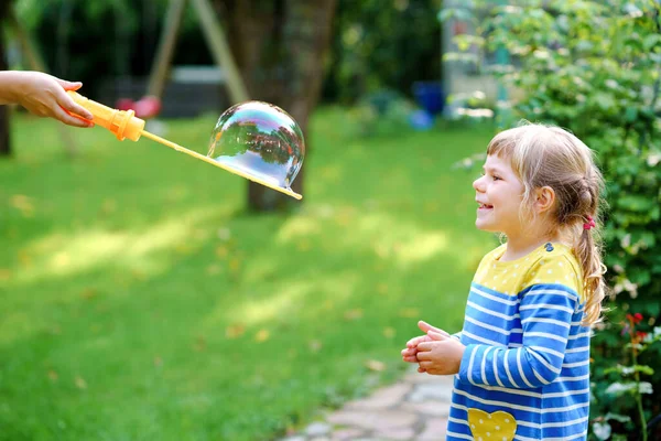 Happy little blonde preschool girl having fun with blowing soap bubble blower. Cute child playing on sunny summer day. Happy active funny healthy kid. Activity for children. — Stock Photo, Image