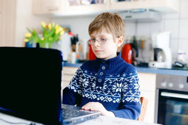 Junge mit Brille lernt zu Hause am Laptop für die Schule. Entzückendes Kind, das Hausaufgaben macht und Notizbuch und moderne Geräte benutzt. Heimschulkonzept. — Stockfoto