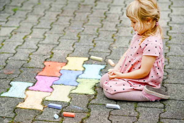 Pequena pintura menina pré-escolar com giz colorido no chão no quintal. Criança feliz positiva desenhando e criando imagens. Atividades criativas ao ar livre no verão. — Fotografia de Stock