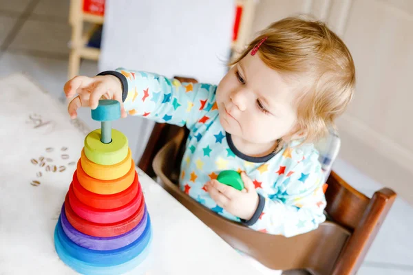 Söt vacker liten flicka leker med pedagogiska leksaker hemma eller på dagis, inomhus. Glad frisk barn har kul med färgglada trä regnbåge leksak pyramid. Grabben lär sig olika färdigheter. — Stockfoto