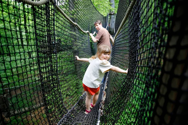 Pequeña niña preescolar y padre caminando por el sendero alto del dosel del árbol con pasarela de madera y cuerdas. Feliz niño y papá activo, joven explorando el camino de la copa de un árbol. Actividad divertida para familias al aire libre —  Fotos de Stock