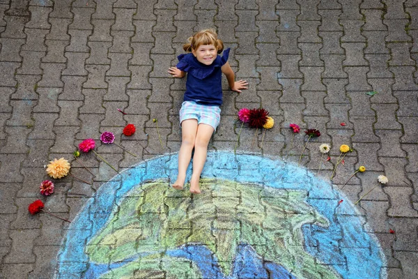 Malá školačka s květinami a barevnými křídy na zemi. Pozitivní batole. Mírový koncept. Tvorba dětí pro záchranu světa, životního prostředí a ekologie. — Stock fotografie