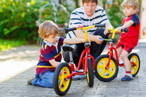 İki mutlu küçük çocuk çocuklar ve babası zinciri üzerinde bisiklet tamir ve denge bisiklet tekerleği değiştirmek — Stok fotoğraf