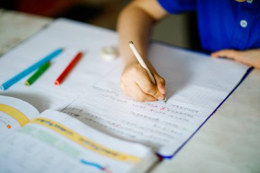 Gözlüklü, ev ödevi yapan, renkli kalemlerle mektup yazan küçük bir çocuğun yakın çekimi. Küçük çocuk içeride egzersiz yapıyor. İlkokul ve eğitim, evde eğitim kavramı..