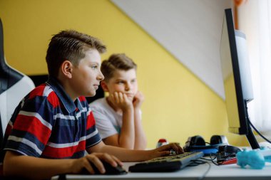 Masaüstü bilgisayarında bilgisayar oyunu oynayan iki çocuk. Çocuklar için modern bağımlılık aktivitesi. Kardeşler ve arkadaşlar evde oyun oynuyorlar..