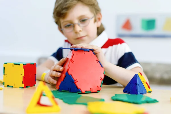 Happy kid boy with glasses having fun with building and creating geometric figures, learning mathematics and geometry — Stock Photo, Image