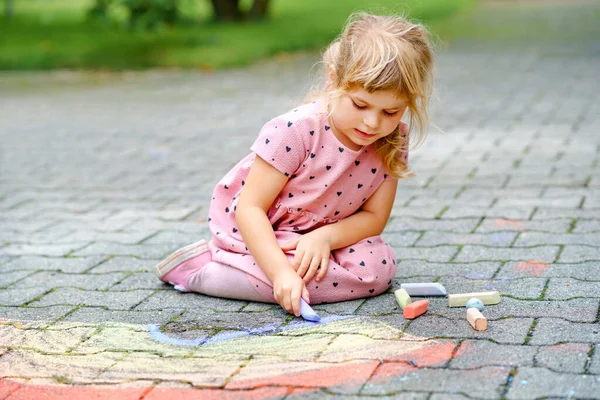 Pequeña niña preescolar pintando arco iris con tiza de colores en el suelo en el patio trasero. Positivo feliz niño pequeño dibujo y la creación de imágenes. Actividad creativa al aire libre en verano. — Foto de Stock