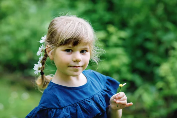 Pequena menina pré-escolar com tranças e flores de margarida em longos cabelos loiros. Close-up da criança. Conceito de verão. Crianças ao ar livre com margaridas flor. Tocando ele me ama. — Fotografia de Stock