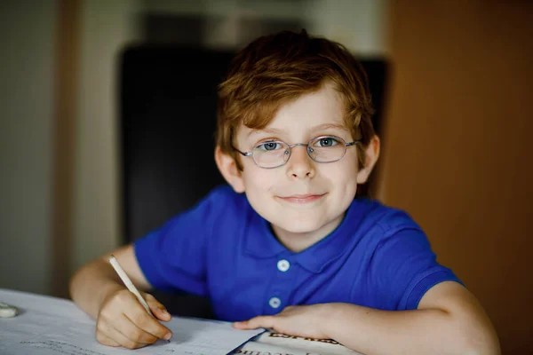 Ritratto di ragazzino con gli occhiali a casa a fare i compiti, scrivere lettere con penne colorate. Un bambino che fa esercizio, in casa. Scuola elementare e istruzione, concetto di istruzione a domicilio. — Foto Stock