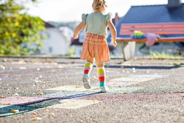 Close-up van leggs van kleine peuter meisje spelen hopscotch spel getrokken met kleurrijke krijtjes op asfalt. Kleine actieve kind springen op speeltuin buiten op een zonnige dag. Zomer activiteiten voor kinderen. — Stockfoto