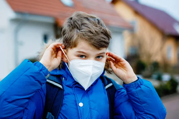 Rapaz a usar máscara médica a caminho da escola. Mochila infantil mochila. Schoolkid no outono frio ou dia de inverno com roupas quentes. Fechamento e tempo de quarentena durante a doença pandémica da coroa — Fotografia de Stock