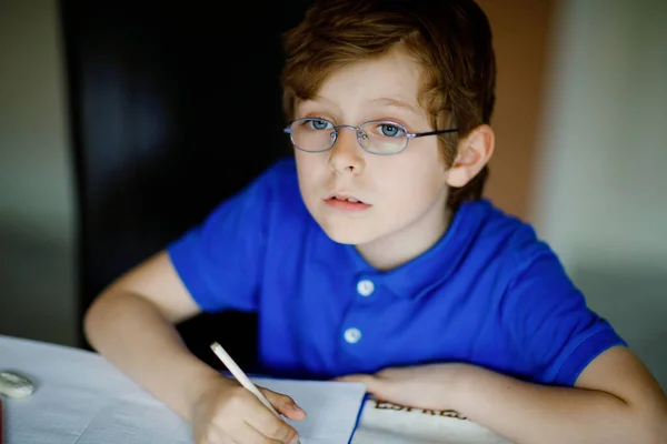 Portret van een kleine jongen met een bril thuis, huiswerk maken, brieven schrijven met kleurrijke pennen. Klein kind aan het sporten, binnen. Basisschool en -onderwijs, thuisonderwijs. — Stockfoto