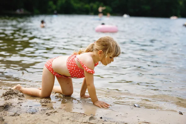 Niña rubia de preescolar divirtiéndose jugando con arena en el lago en el día de verano, al aire libre. Feliz niño aprendiendo a nadar. Ocio activo con niños de vacaciones. Peligro en lagos domésticos — Foto de Stock