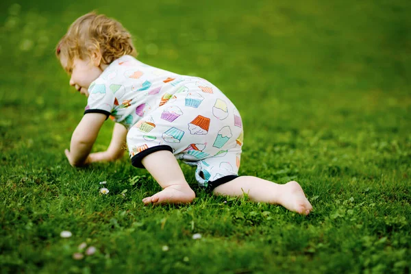 Schattig schattig baby meisje kruipen en maak eerste stappen buiten. Gezond gelukkig peuter kind leren lopen. Mooi meisje genieten lente tuin verkennen wereld. — Stockfoto