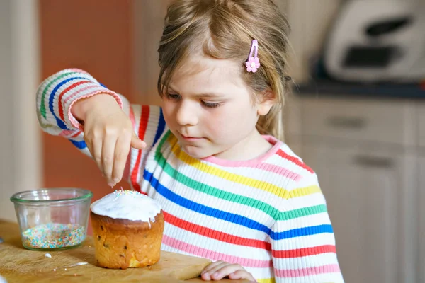 Kleine kleuter meisje versieren traditionele paastaart genaamd paska in het Russisch en Oekraïens. Gelukkig kind met zoete hagelslag op vakantie. — Stockfoto