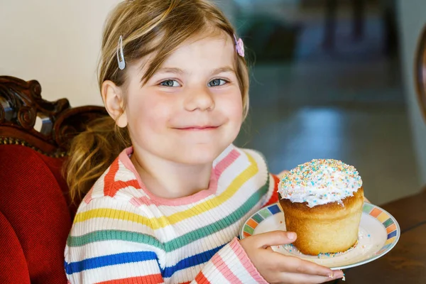 ロシア語とウクライナ語でパスカと呼ばれる伝統的なイースターケーキを飾る小さな就学前の女の子。幸せな子供で甘いスプリンクル休日. — ストック写真