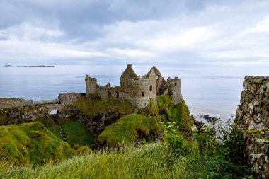 Dunluce Şatosu 'nun kalıntıları, Antrim, Kuzey İrlanda, güneşli bir günde yarı bulutlu gökyüzü. Vahşi Atlantik Yolu yakınlarındaki eski İrlanda kalesi.