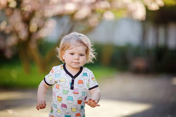 화창한 날에 봄 정원에서 귀여운 아기 여자의 초상화. 아름 다운 행복 미소 핑크 피와 유아 목련 나무 배경에. 건강 한 아이 즐기는 봄 시즌. — 스톡 사진