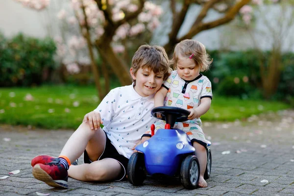 Cute little girl i chłopca szkoły bawiąc się niebieski mały samochód zabawki w ogrodzie domu lub przedszkola. Maluch siostra i brat dzieci dobrze się bawią razem. — Zdjęcie stockowe