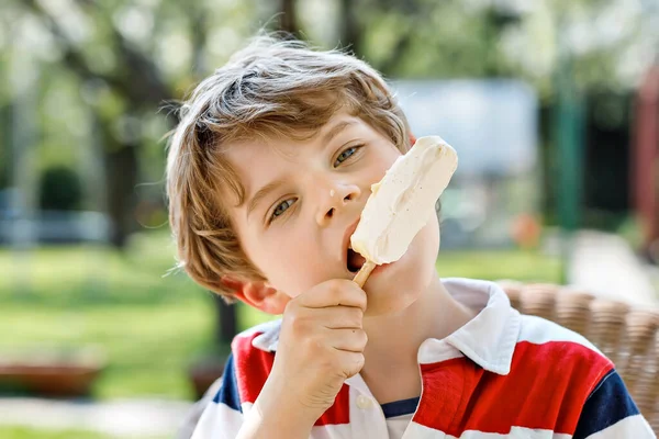 Yazın dondurma yiyen küçük bir anaokulu çocuğu. Soğuk tatlılı mutlu çocuk. Beyaz çikolatalı dondurma. Gülen komik çocuk..