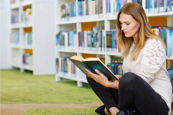 Young beautiful woman in public library, holding, reading and choosing books for leisure or education. Woman making research for college study — Stock Photo, Image