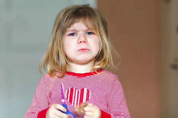Маленькая милая девочка-малышка проводит эксперимент с ножницами и стрижкой волос. Забавная малышка сама режет пони дома. Трофей — стоковое фото