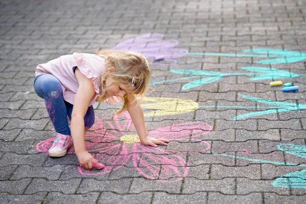 Kleine Vorschulmädchen malen mit bunten Kreiden Blumen auf dem Boden im Hinterhof. Positiv glückliches Kleinkind zeichnet und schafft Bilder auf Asphalt. Kreative Aktivitäten für Kinder im Sommer. — Stockfoto