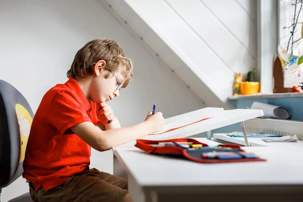 Портрет маленького мальчика в очках дома, который делает домашнее задание, пишет и учится. Маленький ребенок занимается спортом в помещении. Начальная школа и образование, концепция домашнего обучения. — стоковое фото