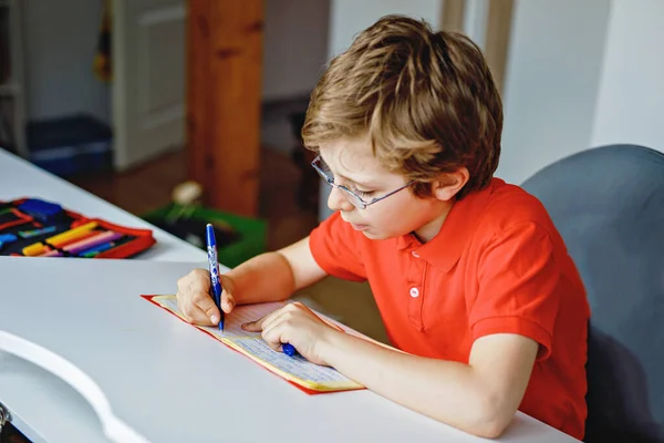 Ritratto di ragazzino con gli occhiali a casa che fa i compiti, scrive e impara. Un bambino che fa esercizio, in casa. Scuola elementare e istruzione, concetto di istruzione a domicilio. — Foto Stock