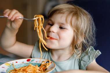 Küçük tatlı kız domatesli makarna ve kıymalı bolonez yiyor. Anaokulundaki mutlu çocuk evde, evde, erişte ve sebzelerle taze pişmiş sağlıklı yemek yiyor..