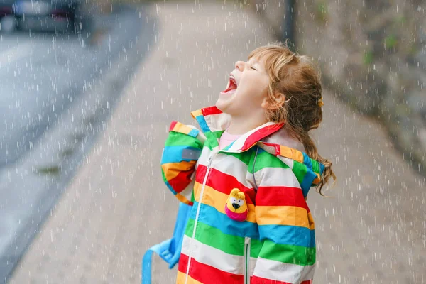 Портрет маленькой девочки в дождливый день. Счастливый позитивный ребенок бежит под дождем, лужи. Дошкольник в дождевой одежде ловит капли дождя. Активность детей в день плохой погоды. — стоковое фото