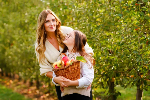 Happy school girl and beautiful mother with red apples in organic orchard. Happy woman and kid daughter picking ripe fruits from trees and having fun in garden. Harvest season for family. — Stock Photo, Image