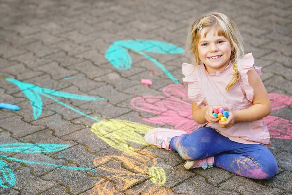 Pequeña pintura de niña preescolar con tiza de colores flores en el suelo en el patio trasero. Positivo feliz niño pequeño dibujo y la creación de imágenes sobre asfalto. Creativa actividad infantil al aire libre en verano. — Foto de Stock