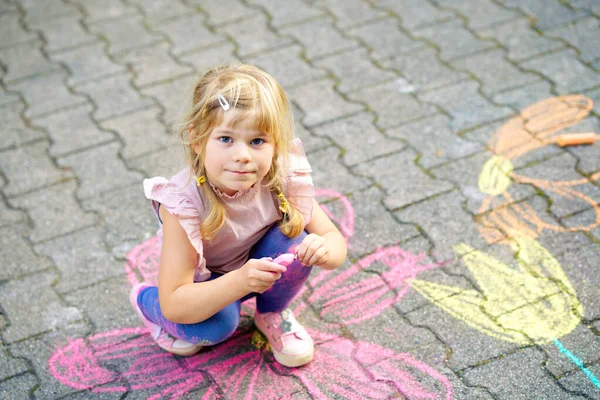 미취학 아동 이 뒷마당 땅에 화려 한 분필로 꽃을 꽂고 그림을 그리고 있다. 행복 한 아이들 이 아스팔트 위에서 그림을 그리고 그림을 그리는 것이죠. 여름에 야외에서 아이들이 하는 창의적 인 활동. — 스톡 사진