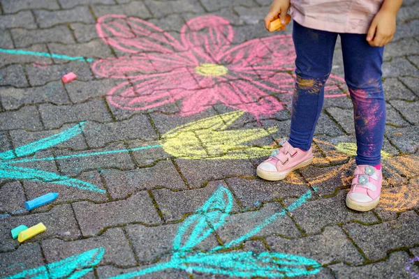 Liten förskola flicka målning med färgglada kritor blommor på marken på bakgården. Positivt glad barn rita och skapa bilder på asfalt. Kreativa utomhus barn aktivitet på sommaren. — Stockfoto
