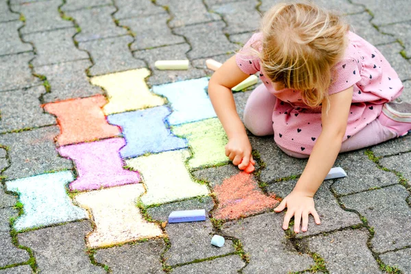 Arka bahçesinde renkli tebeşirlerle resim yapan küçük bir anaokulu kızı. Çocuk resim çizerken ve resim çizerken çok mutlu. Yazın yaratıcı açık hava aktivitesi. — Stok fotoğraf