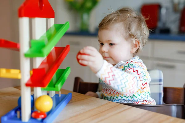 Küçük kız evde ya da çocuk odasında eğitici oyuncaklarla oynuyor. Mutlu sağlıklı çocuk renkli tahta top pisti ile eğleniyor. Çocuk top tutmayı ve yuvarlanmayı öğreniyor. Motorik eğitim.