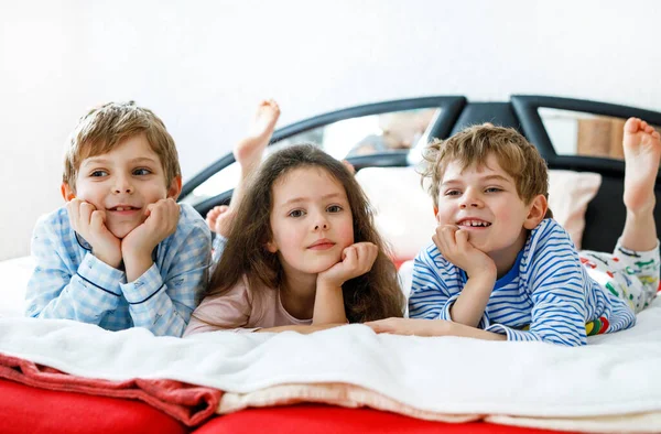 Drie gelukkige kinderen in pyjama 's die een pyjamafeest vieren. kleuterschool en school jongens en meisje hebben plezier samen — Stockfoto