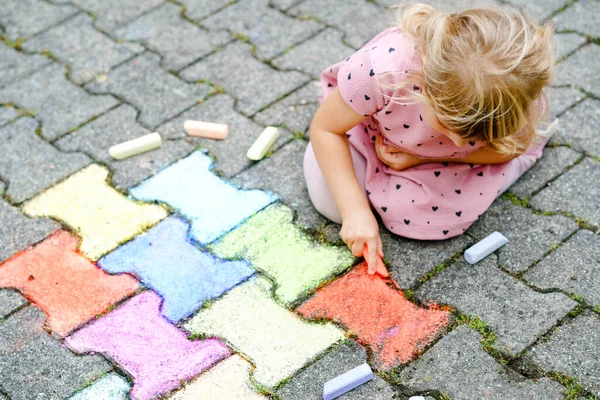 Arka bahçesinde renkli tebeşirlerle resim yapan küçük bir anaokulu kızı. Çocuk resim çizerken ve resim çizerken çok mutlu. Yazın yaratıcı açık hava aktivitesi.