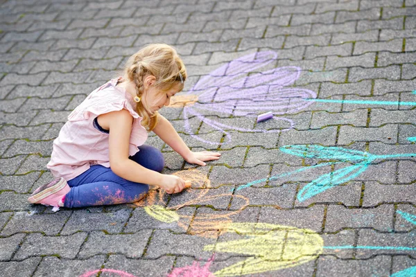 Pequena pintura menina pré-escolar com giz colorido flores no chão no quintal. Criança feliz positiva desenhando e criando imagens no asfalto. Atividades criativas de crianças ao ar livre no verão. — Fotografia de Stock