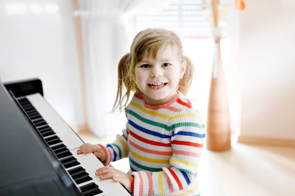 Hermosa niña tocando el piano en la sala de estar. Lindo niño preescolar que se divierte con el aprendizaje de tocar el instrumento de música con el concepto de aprendizaje durante el bloqueo del virus de la corona de educación en casa. —  Fotos de Stock