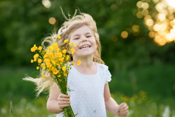 Adorable linda niña preescolar en una flor de diente de león en la naturaleza en el verano. Feliz niño hermoso niño sano con flores, divirtiéndose. Luz de puesta de sol brillante, niño activo. — Foto de Stock