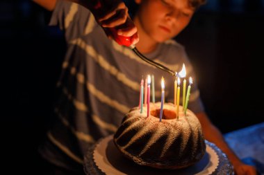 Mutlu sarışın çocuk doğum gününü kutluyor. Çocuk ev yapımı kek üzerine mum üflüyor, kapalı alanda. Okul çocukları için doğum günü partisi, aile kutlaması.