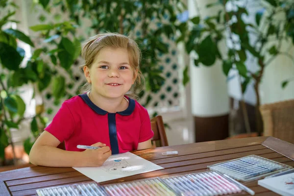 stock image Happy preschool girl learning painting with colorful pencils and felt pens. Little toddler drawing at home on sunny summer day, using colorful feltpens. Creative activity for children