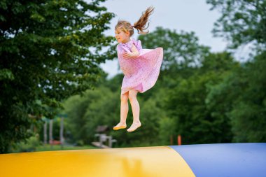 Little preschool girl jumping on trampoline. Happy funny toddler child having fun with outdoor activity in summer. Sports and exercises for children. Trampolin in ukrainian flagg colors. clipart