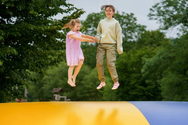 Little preschool girl and school sister jumping on trampoline. Happy funny children, siblings in love having fun with outdoor activity in summer. Trampolin in ukrainian flagg colors.