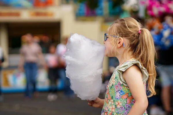 遊園地で綿菓子を食べる愛らしい少女 夏の晴れた日に屋外で眼鏡と大きなキャンディーフロスを持つ幸せな就学前の子供 — ストック写真