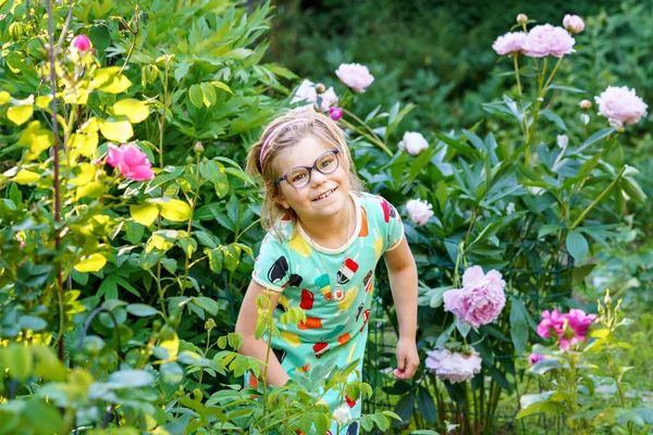 牡丹の花と国内庭でかなり小さな女の子の夏の肖像画 幸せな笑顔の未就学児 自然の愛 ロマンチックな気分と子供を助ける — ストック写真